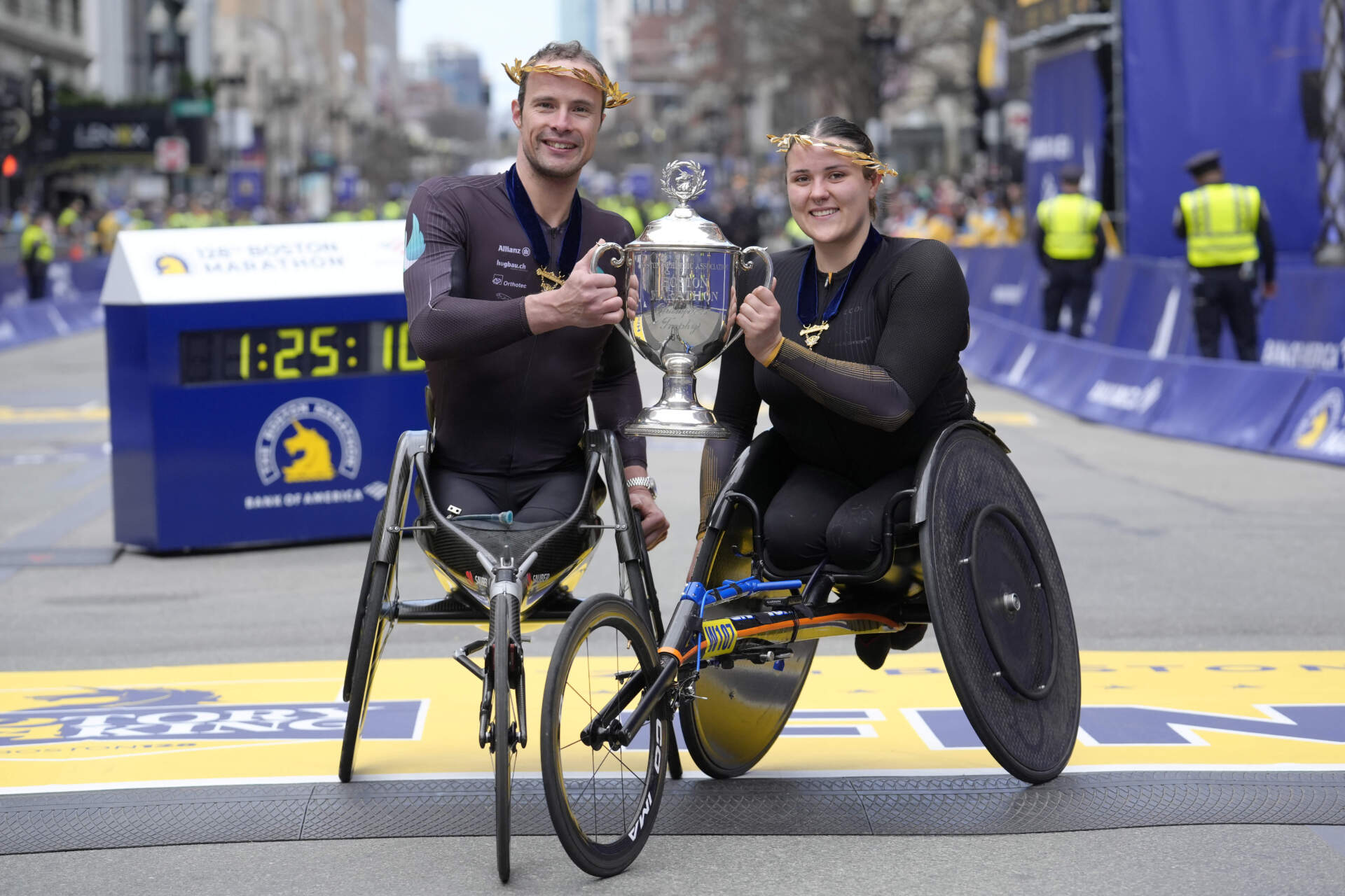 Marcel Hug, of Switzerland, left, winner of the Boston Marathon men's wheelchair division, left, and Eden Rainbow Cooper, of Britain, right, winner of the women's wheelchair division, display the trophy on the finish line in Boston. (Steven Senne/AP)