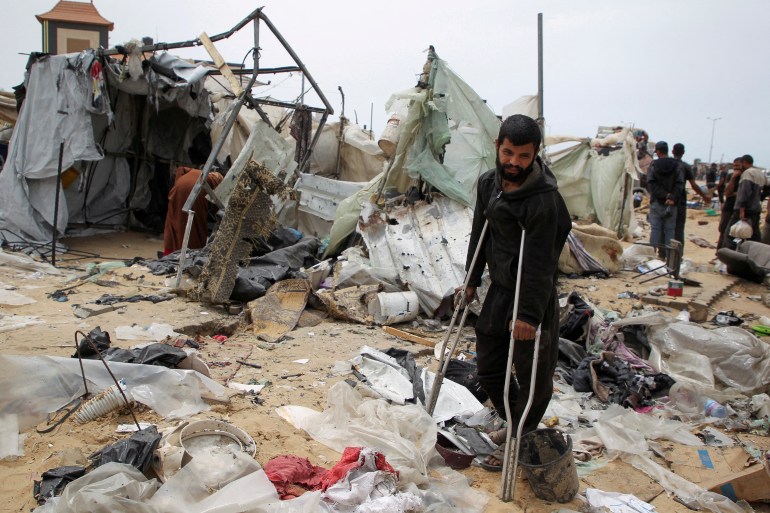 A man looks on as Palestinians inspect a tent camp damaged in an Israeli strike during an Israeli military operation, in Rafah, in the southern Gaza Strip