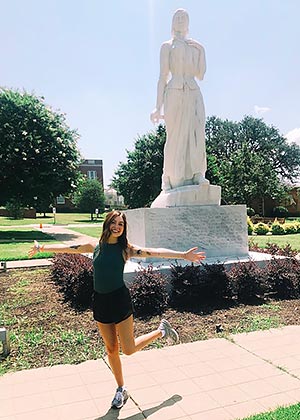 student stands with arms out in front of Minerva statue