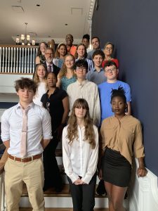 A group of student awardees stand smiling in front of a large staircase in the Townsend Building in Dover.