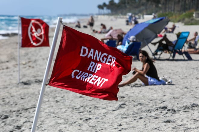 Lifeguards post hazardous rip current flags in the sand on March 22, 2022, at Midtown Beach in Palm Beach, Florida, after making a rescue in the rough surf.