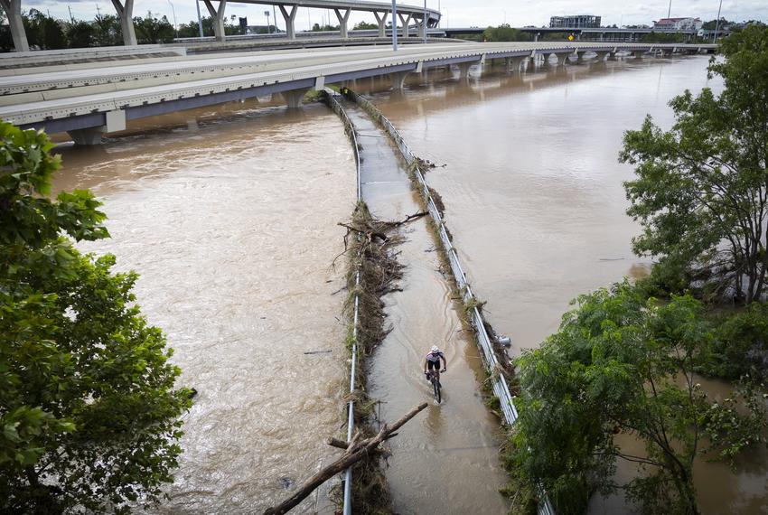 A man cycles across a bridge over a flooded Whiteoak Bayou from Hurricane Beryl on Monday, July 8, 2024, in Houston.