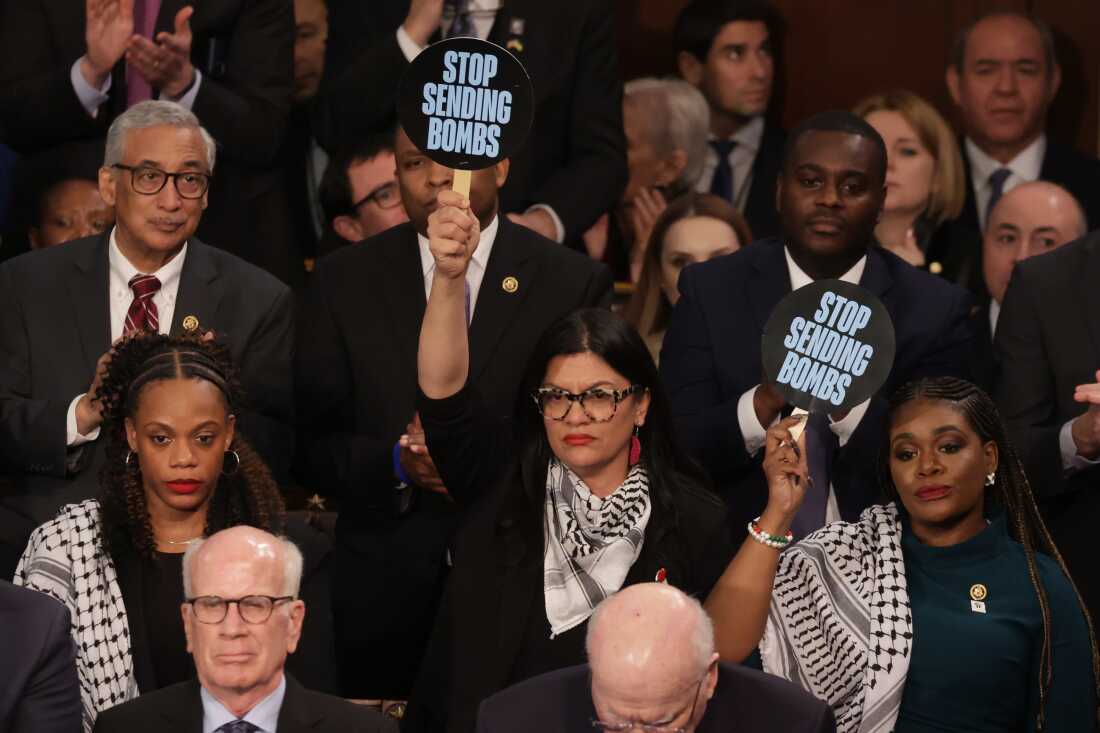 U.S. Rep. Rashida Tlaib, D-Mich., (center) and Rep. Cori Bush, D-Mo., hold up signs as President Biden delivers the State of the Union address on March 7.