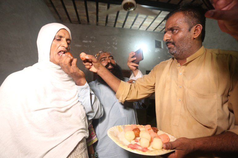 Family members offer sweets to Razya Parveen (L), the mother of Pakistani athlete Arshad Nadeem after his win in the men's javelin throw final of the athletics event at the Paris 2024 Olympic Games, at Mian Channu in Khanewal District on August 9, 2024. - Pakistan's Arshad Nadeem won the Olympic men's javelin title in Paris on August 8, his country's first individual gold at a Summer Games. (Photo by Shahid Saeed MIRZA / AFP)