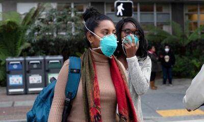 Two Black women stand outside wearing blue N95 face masks.