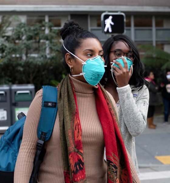 Two Black women stand outside wearing blue N95 face masks.