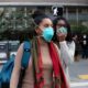 Two Black women stand outside wearing blue N95 face masks.